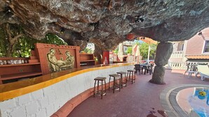 Zona de bar al aire libre con pared de piedra, taburetes y una piscina.