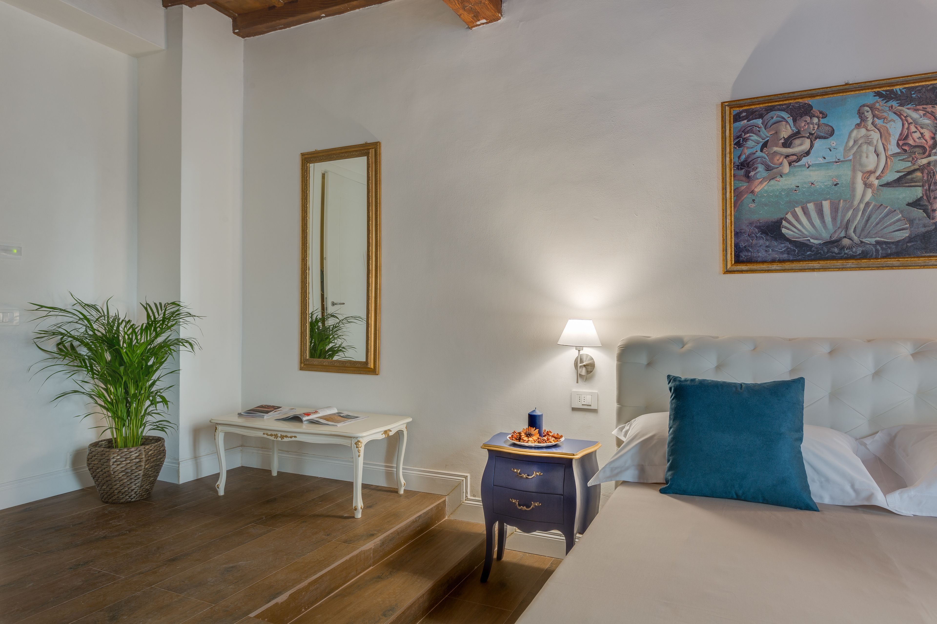 A bedroom with a bed, a nightstand, a lamp, a mirror, and a painting.