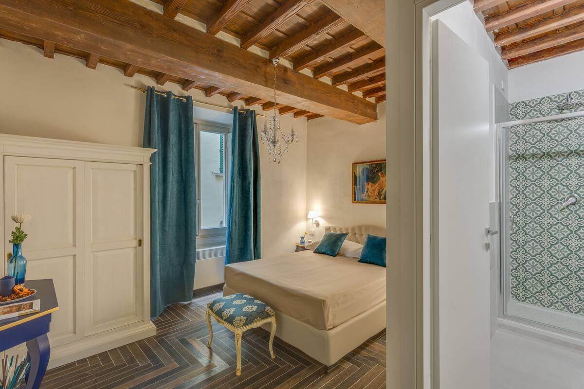Une chambre avec un plafond en bois, un lit avec une literie bleue, une table de chevet, une chaise et une porte avec du verre décoratif.