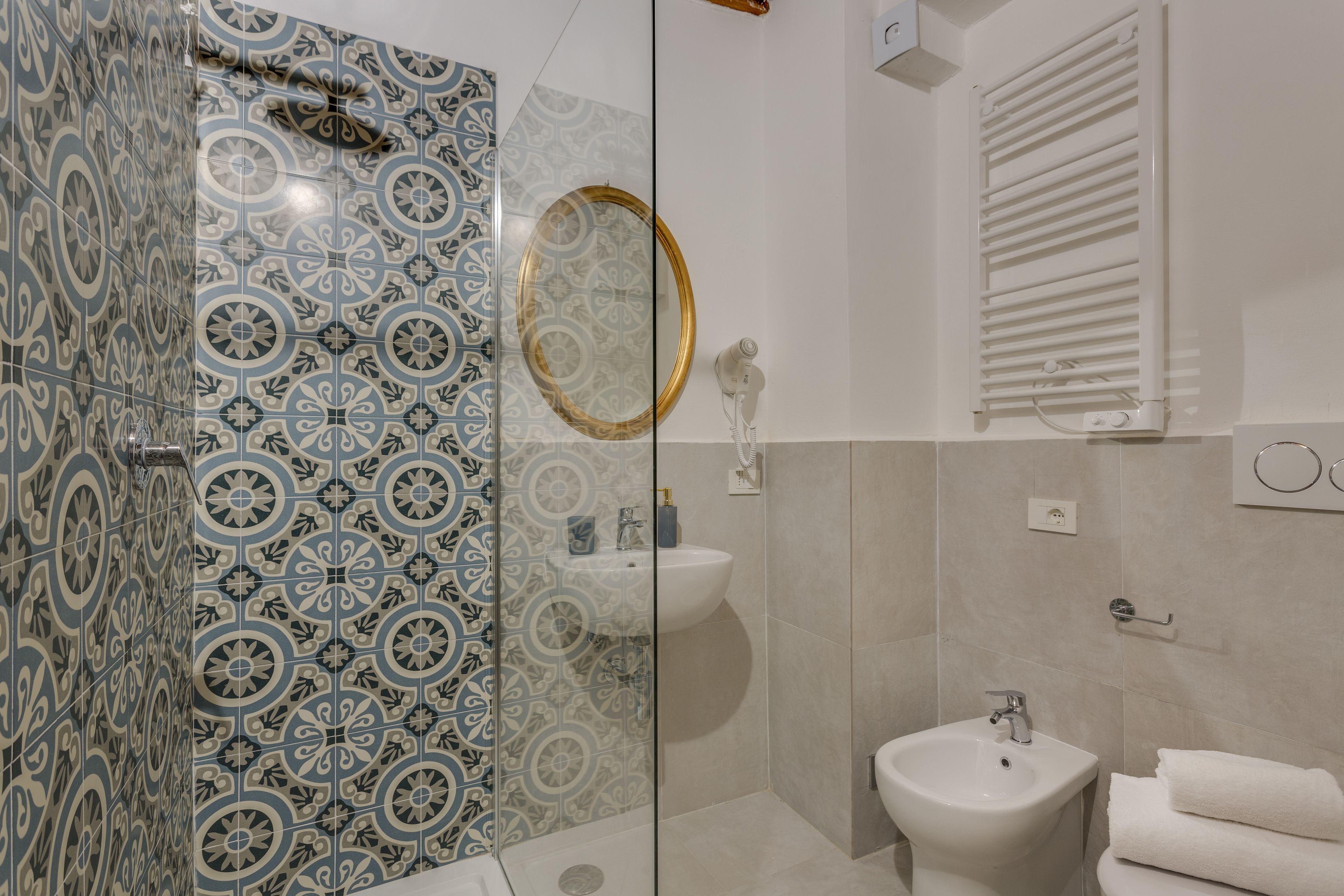 Un bagno con piastrelle decorate, cabina doccia in vetro, lavandino, bidet e porta asciugamani.