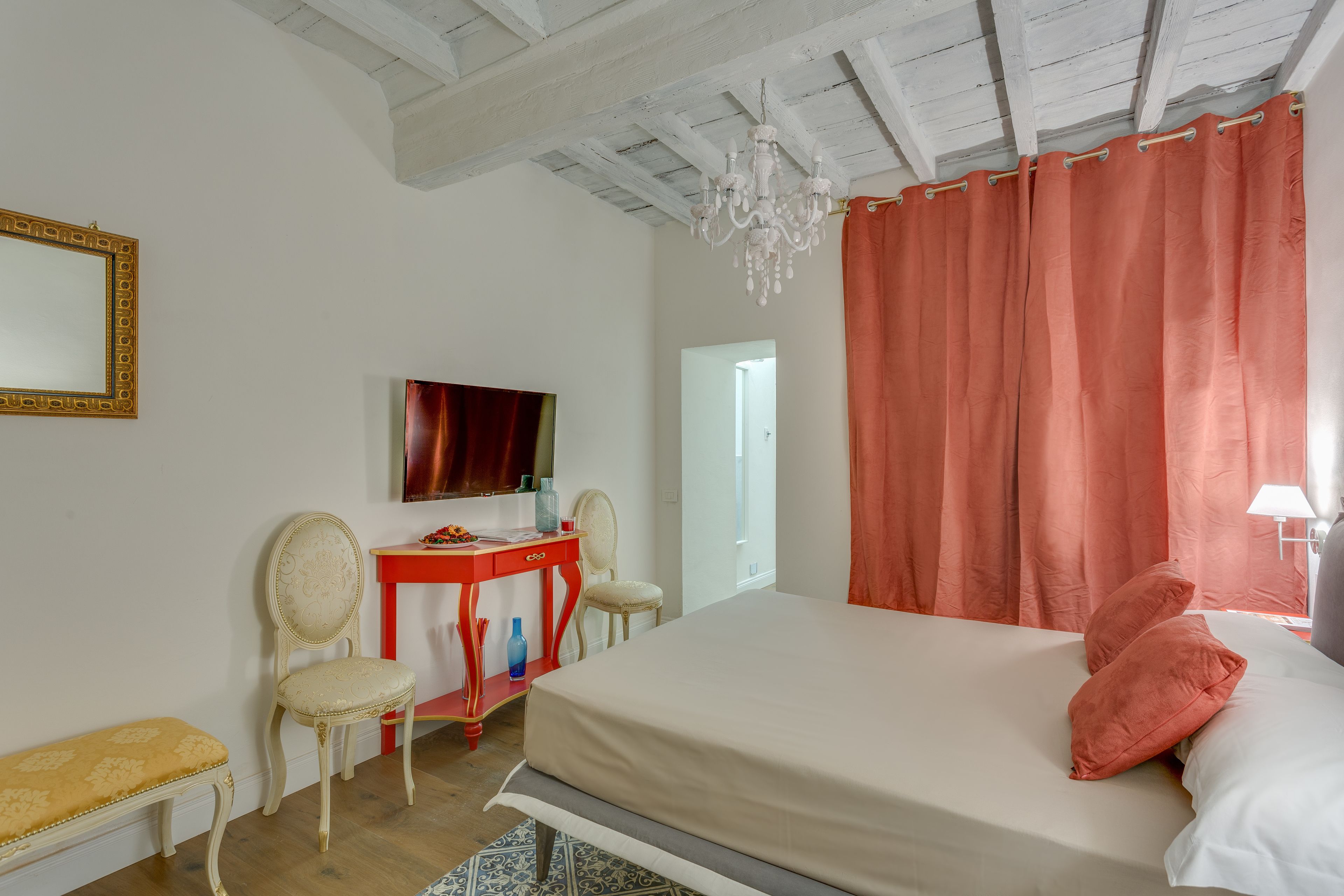 Quarto com cama, escrivaninha, duas cadeiras, espelho e lustre.