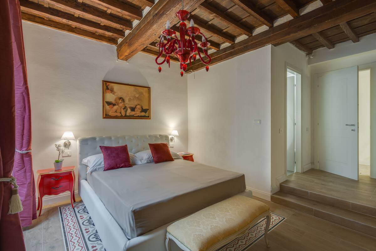 Une chambre à coucher avec un lit, des tables de chevet, un lustre, un tableau et un escalier.