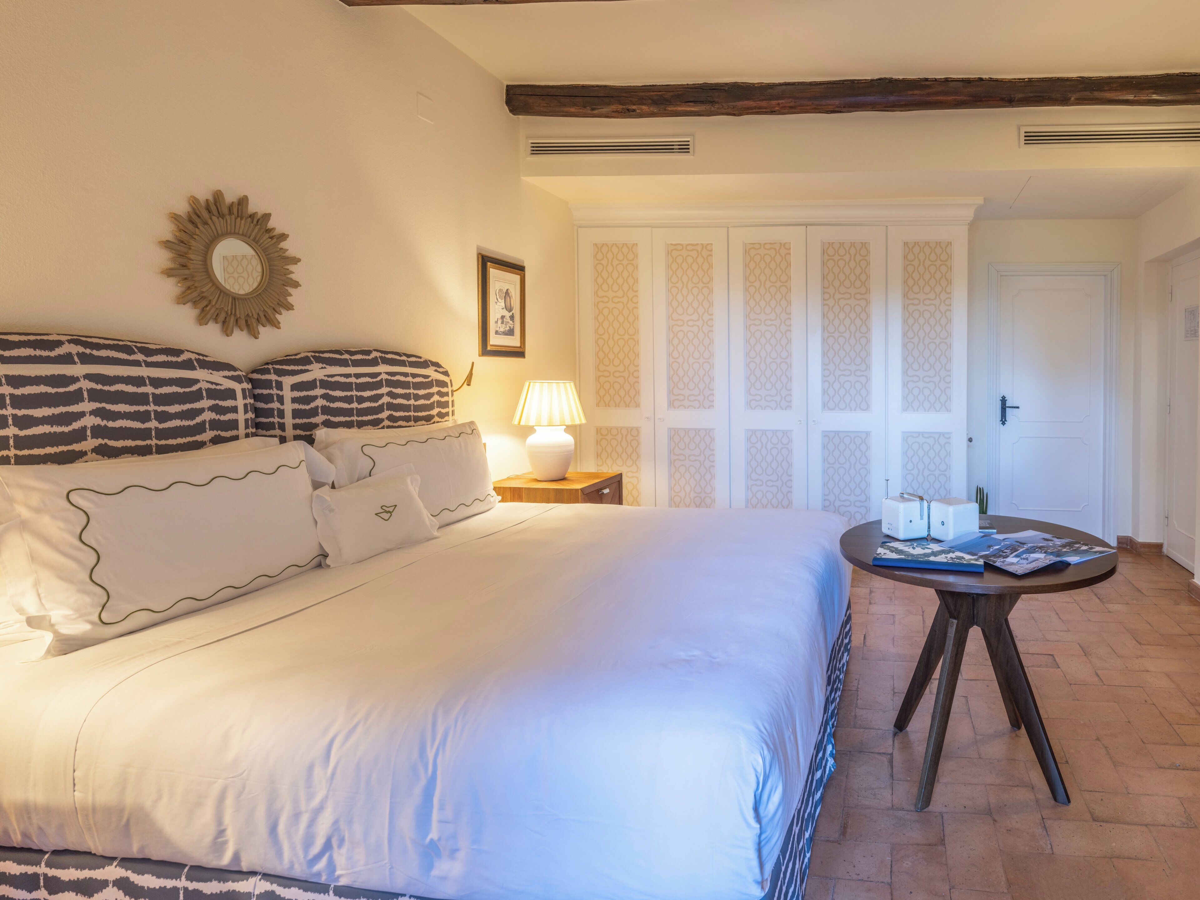 Une chambre à coucher avec un lit, une table de chevet avec une lampe, une petite table avec un livre et une porte à panneaux décorés.