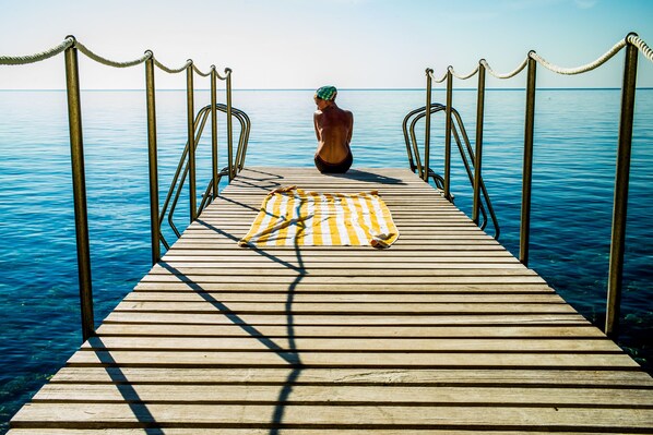 A wooden pier extending into calm blue water, with a striped towel laid out on the deck. - Hotel Il Pellicano (Monte Argentario)