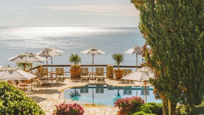 Zona junto a la piscina con sillones de descanso y sombrillas, vista despejada del mar y un jardín bien cuidado.
