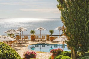 A poolside area with lounge chairs and umbrellas, a clear view of the sea, and a well-maintained garden. - Hotel Il Pellicano (Monte Argentario)