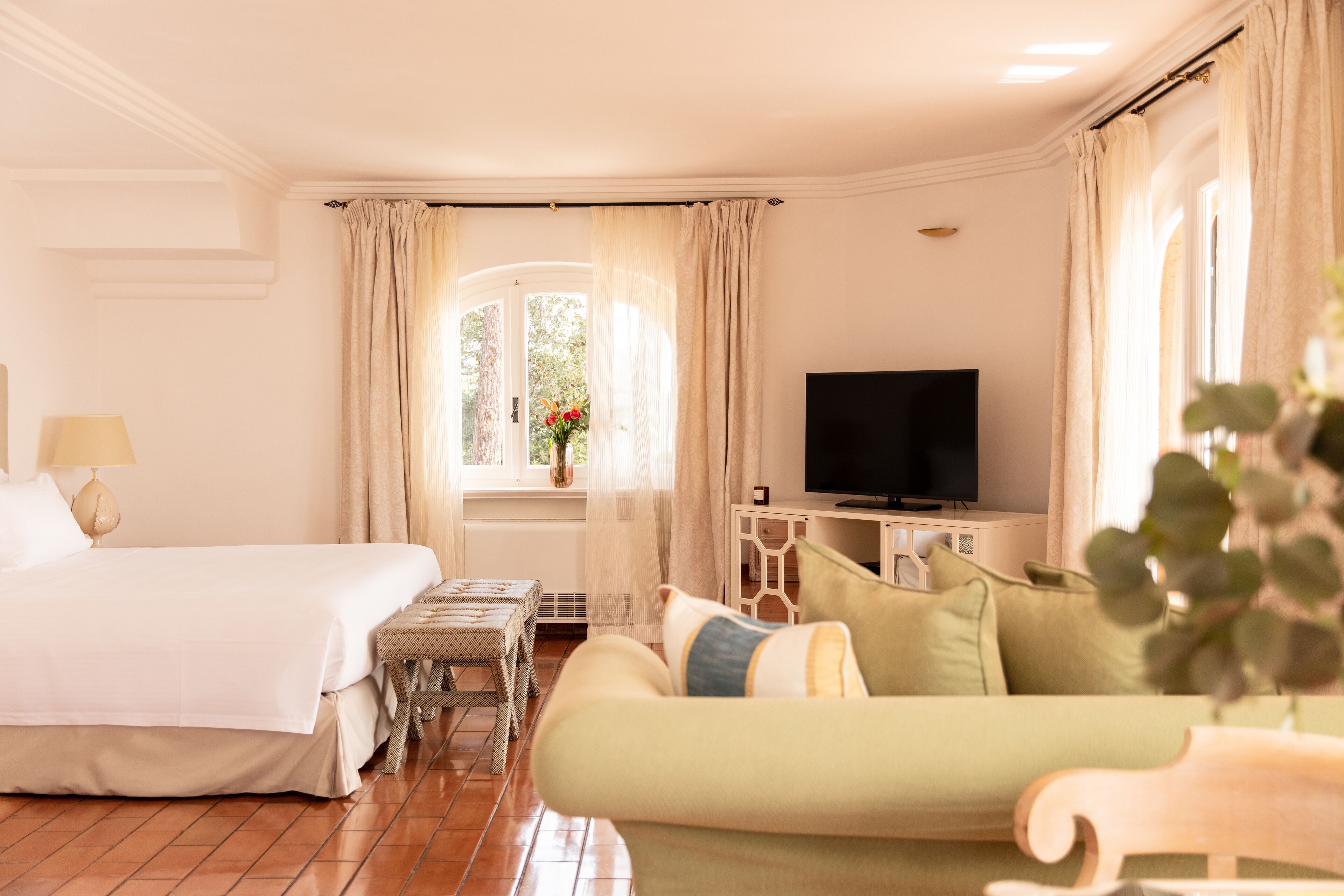 Habitación de hotel con cama, sofá, televisor, una mesita y ventana con cortinas.