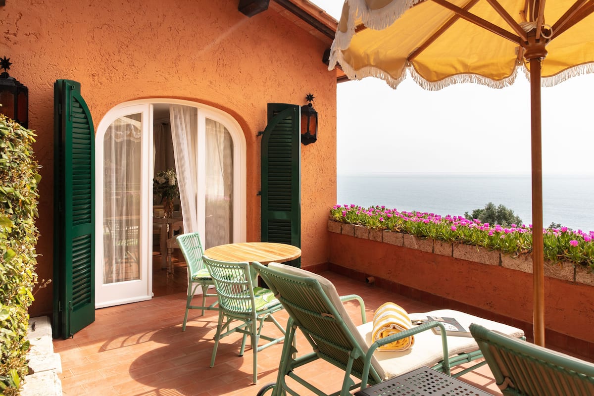 A terrace with a table and chairs, a yellow umbrella, and a view of the sea.