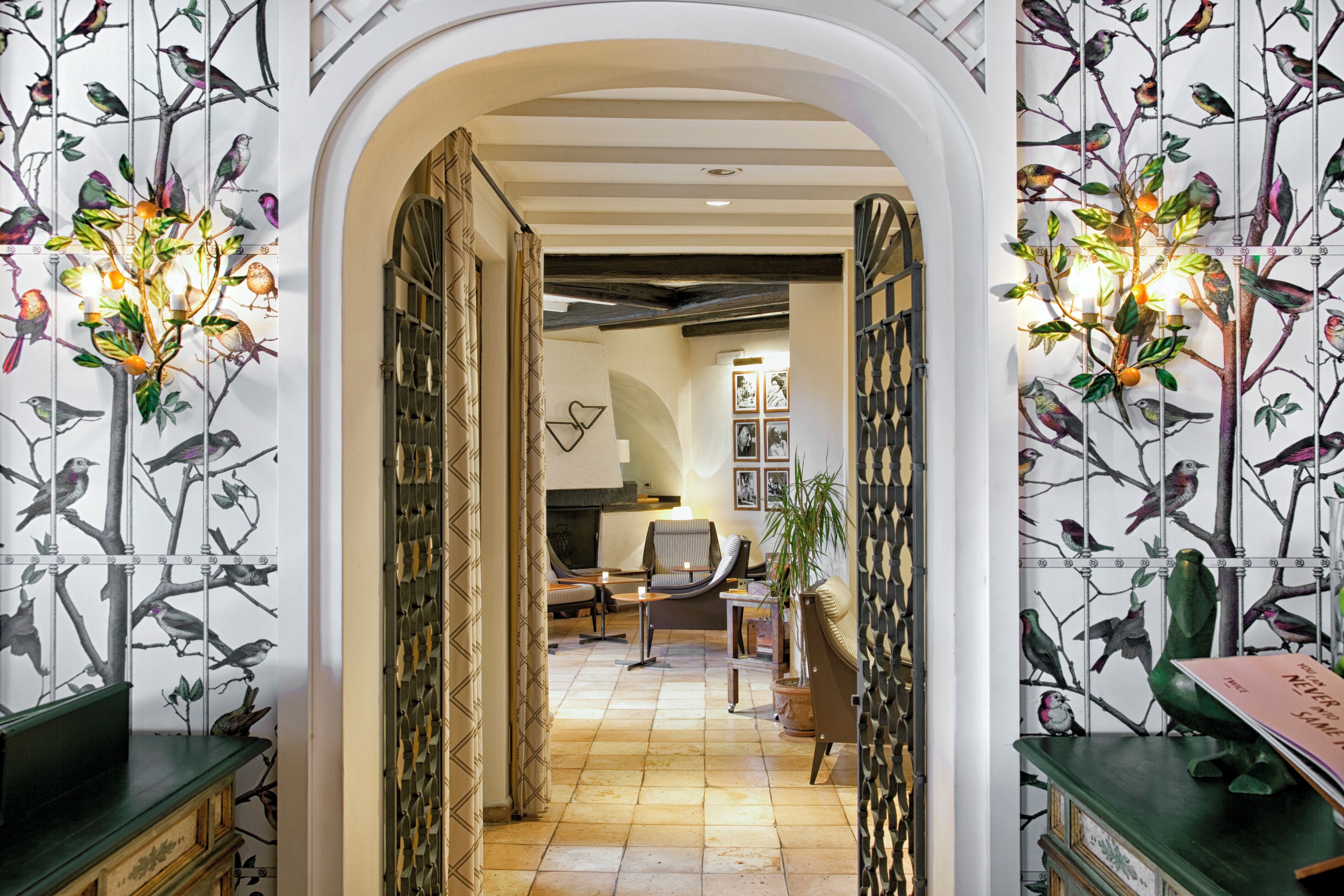 An interior with a hallway leading to a seating area, decorated with bird-themed wallpaper and wall-mounted lighting.