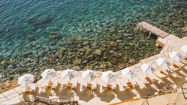 Un hotel frente a la playa con aguas cristalinas, sillas de sol y sombrillas.