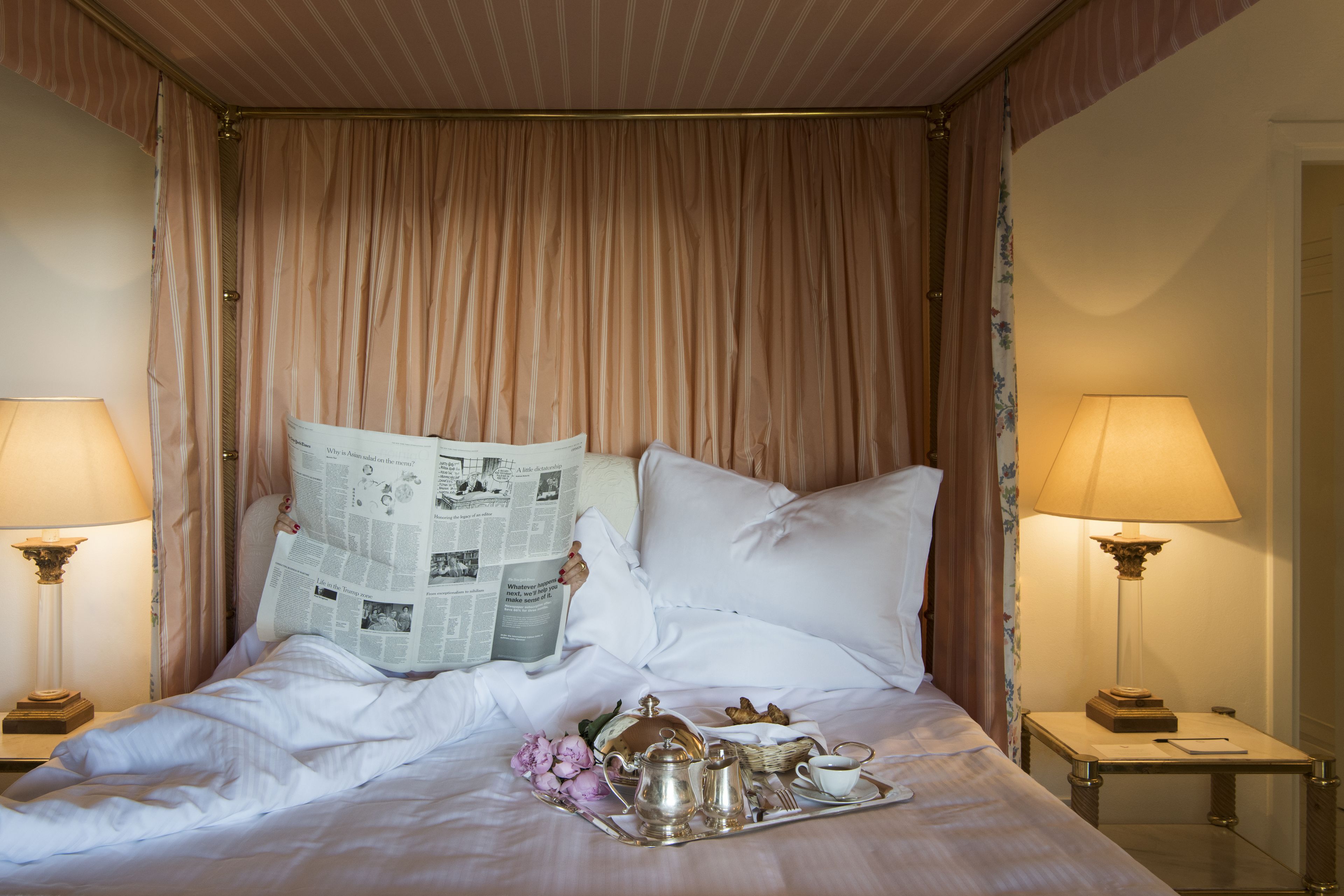 Un letto rifatto con cura, un vassoio con prodotti per la colazione, un giornale e una lampada su entrambi i lati.
