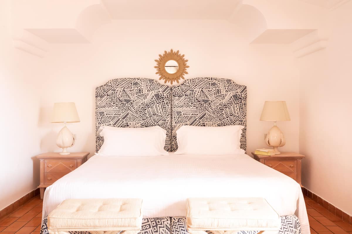 A bed with a patterned headboard, two bedside tables with lamps, and a sun-shaped decoration above the headboard.