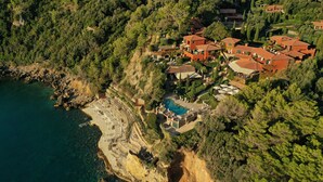 Vista aérea de una propiedad costera con varias construcciones, una piscina y un litoral rocoso.