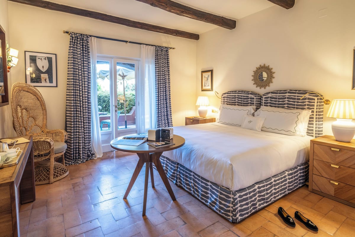 A bedroom with a bed, a chair, a table, and a nightstand.