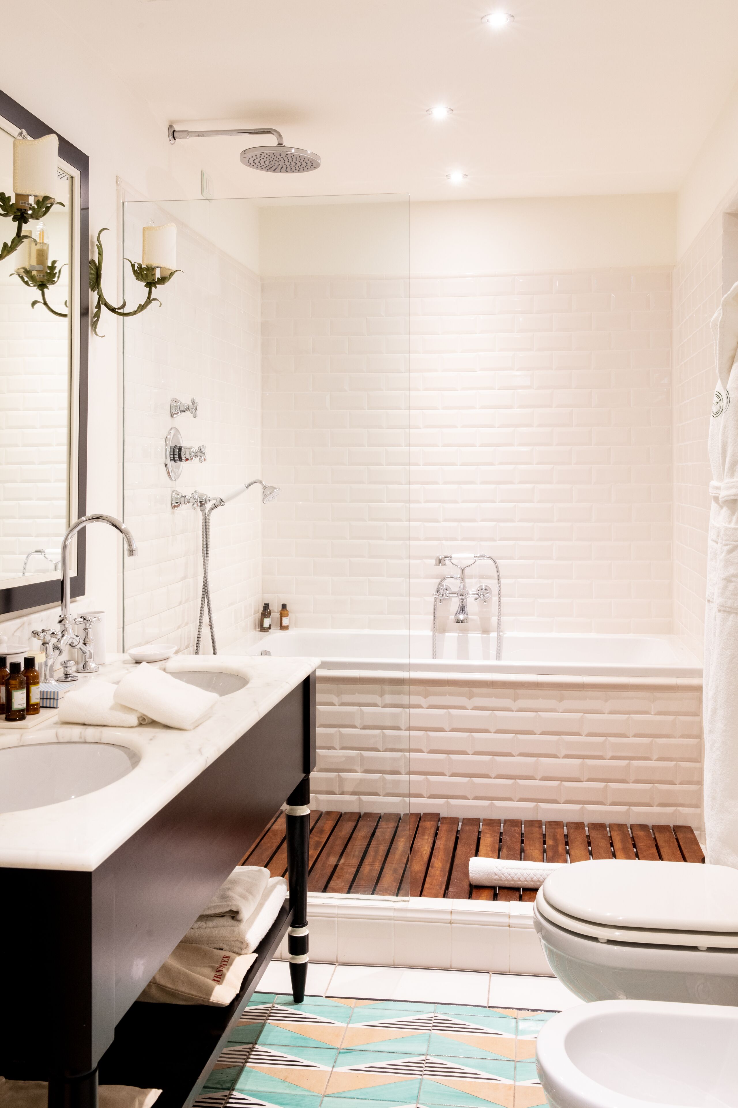 A modern bathroom with a large mirror, two sinks, a bathtub, and a toilet.