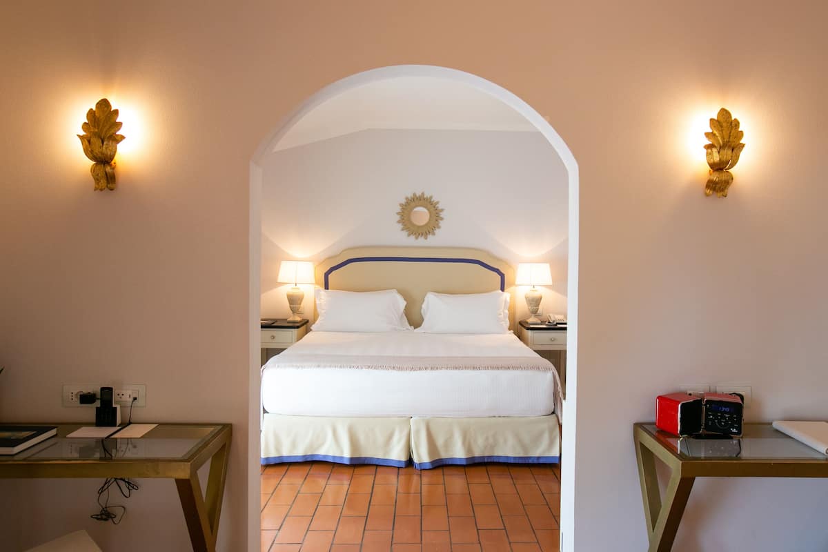 A hotel room with a bed, two bedside tables, a desk, and a wall-mounted clock.