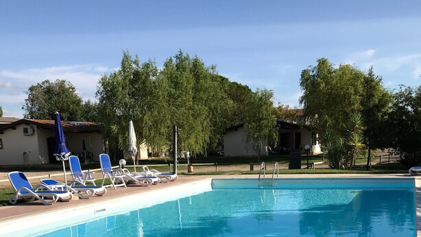 Una piscina rectangular con agua azul cristalina, rodeada por un solárium con baldosas. Varias sillas de descanso azules están dispuestas a lo largo de la piscina.