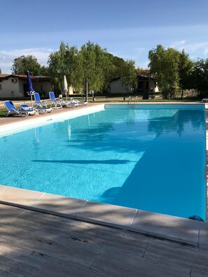 A rectangular swimming pool with clear blue water, surrounded by a tiled deck. There are several blue lounge chairs aligned along the poolside. - Agriturismo Arcobaleno (Grosseto)