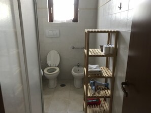 A small bathroom with a toilet, bidet, and a shelf with towels and toiletries. - Agriturismo Arcobaleno (Grosseto)