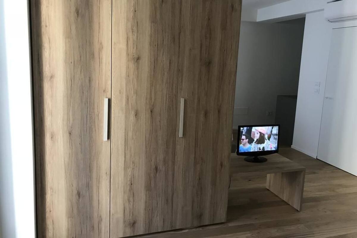 Una habitación moderna con un armario de madera, un televisor de pantalla plana sobre un soporte y un banco de madera.