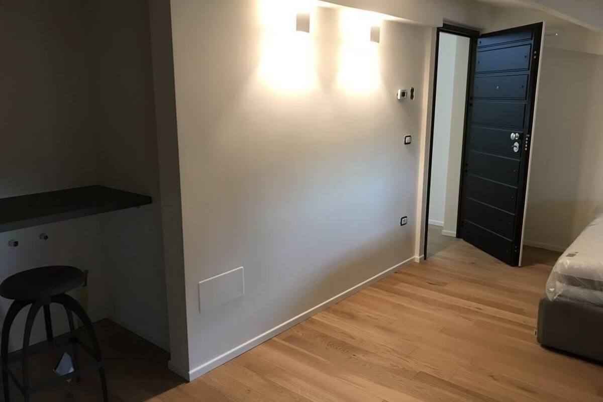 Una habitación moderna con piso de madera, una puerta negra y un taburete pequeño.