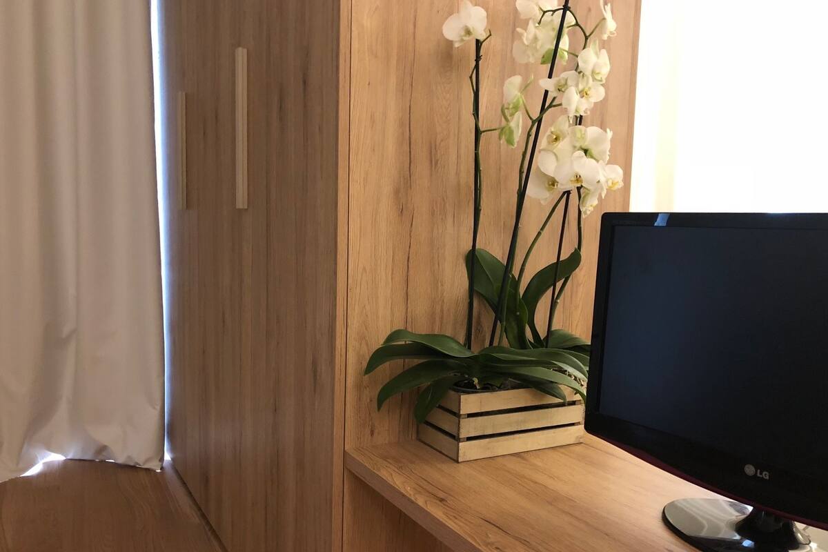Un escritorio de madera con un monitor de computadora, una planta de orquídea blanca en una caja de madera y un armario de madera.