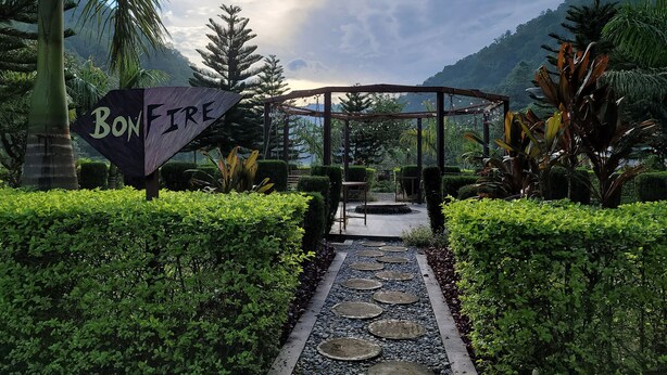 Un sentier mène à une pergola en bois sur laquelle est accrochée une pancarte indiquant « FEU DE JOIE ».