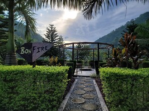 Un sentier mène à une pergola en bois sur laquelle est accrochée une pancarte indiquant « FEU DE JOIE ».