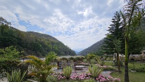 Un jardin aménagé avec un espace de détente, entouré d’une végétation luxuriante et offrant une vue sur un paysage montagneux.