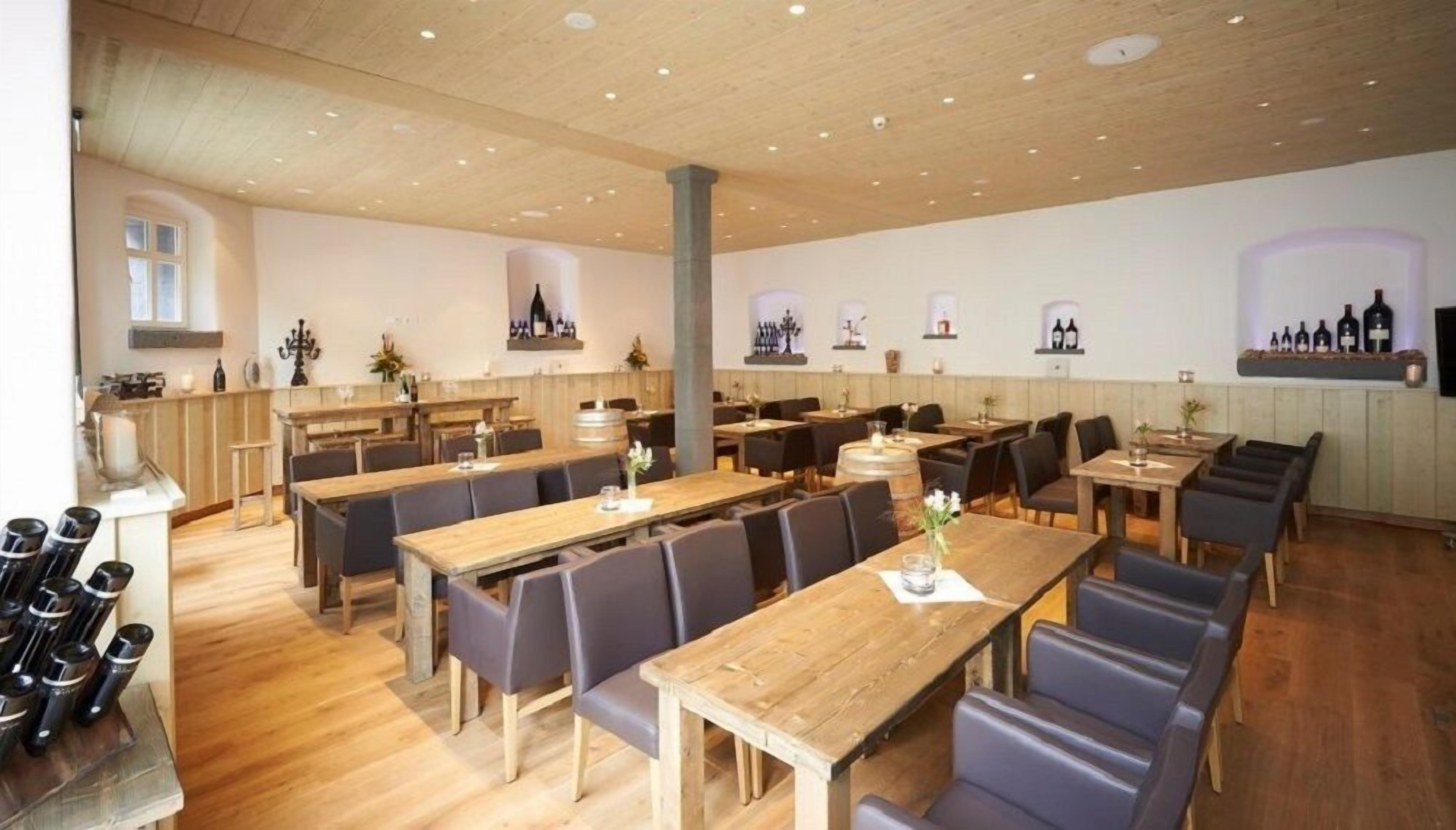 Un restaurante con mesas y sillas de madera, una zona de bar y botellas de vino expuestas en la pared.