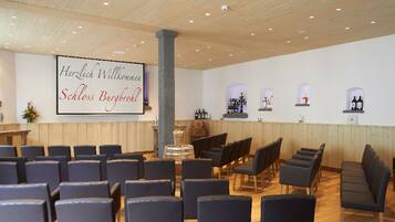 A conference room with rows of chairs, a wooden reception desk, and a wall-mounted screen displaying text.