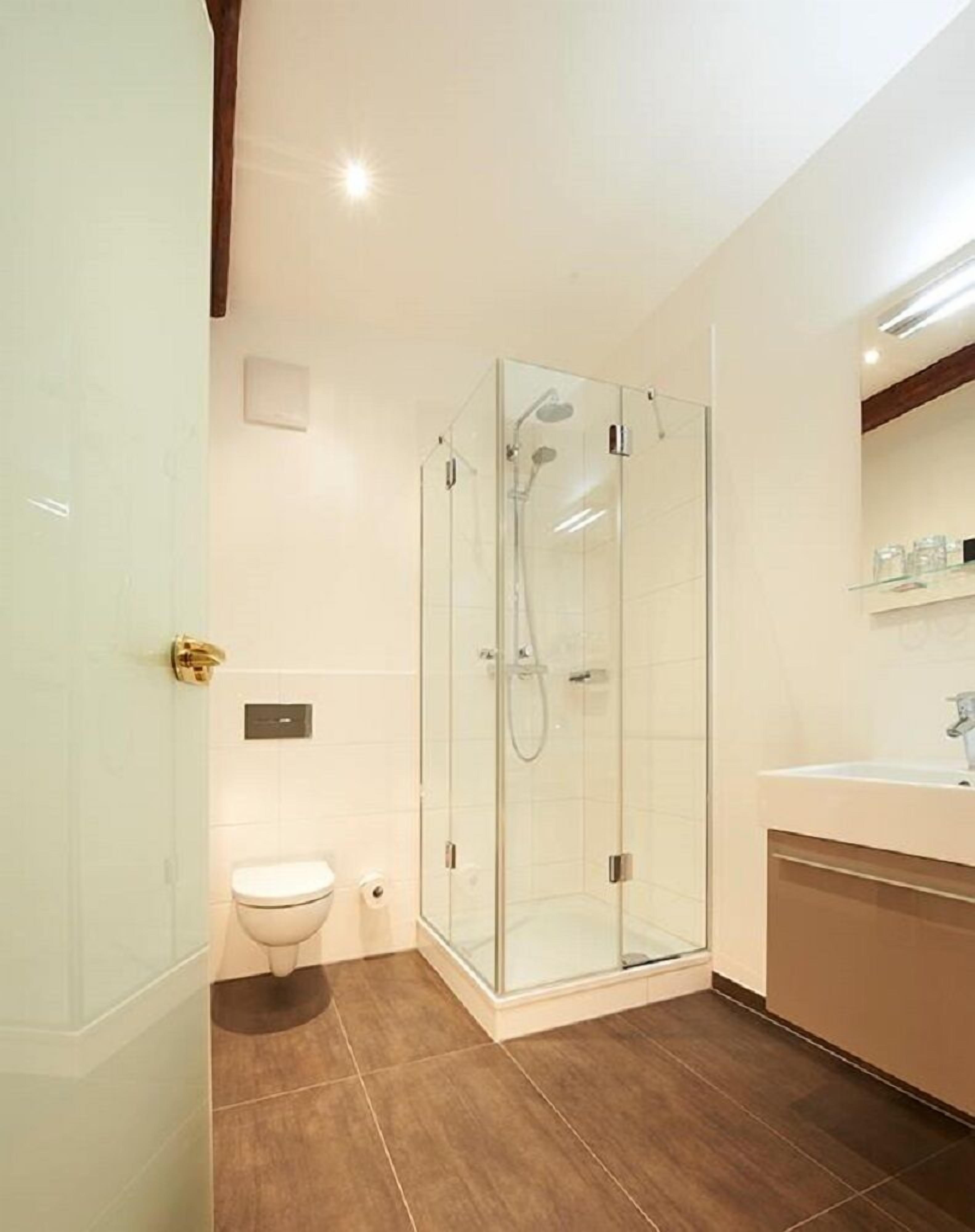 Un baño moderno con ducha acristalada, inodoro y lavabo con espejo.