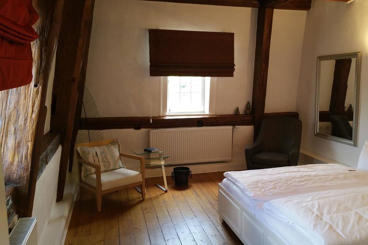 Un dormitorio con cama, una silla, una mesita, un radiador y una ventana con persiana.