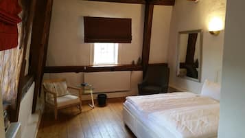 Een slaapkamer met een bed, een stoel, een kleine tafel, een radiator en een raam met een jaloezie.
