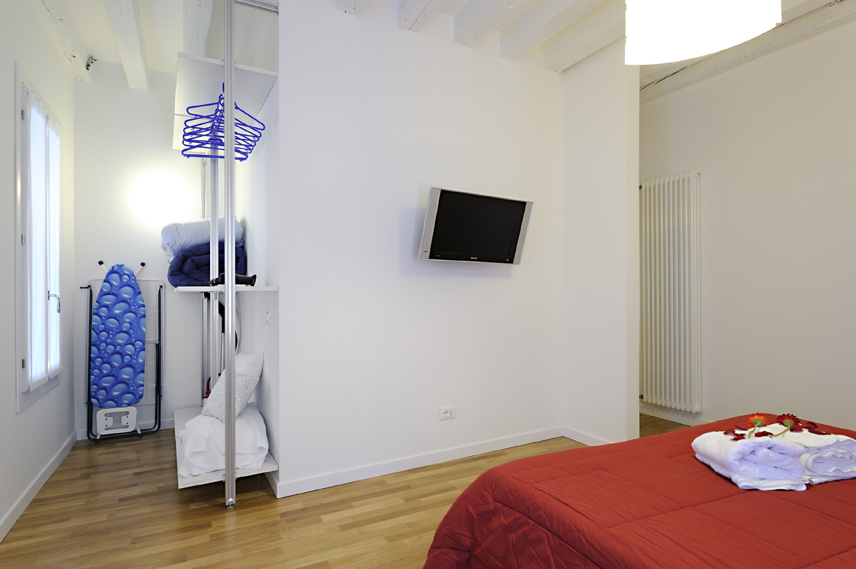 A hotel room with a bed, a television, a radiator, and a blue ironing board.