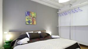 A neatly made bed with a white and brown quilt, a colorful abstract painting on the wall, and a white wardrobe with blue hangers. - Rialto Al Manganer (Venice)