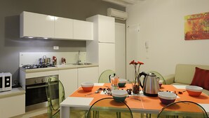 A compact kitchen with white cabinets, a gas stove, and a dining area with a table set for two. - Rialto Al Manganer (Venice)