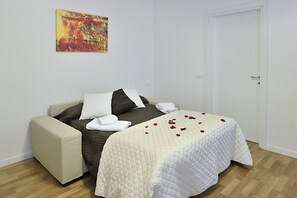 A neatly made bed with a white quilt and red rose petals, a beige armchair, and a colorful abstract painting on the wall. - Rialto Al Manganer (Venice)