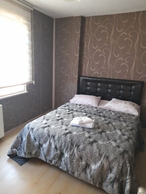 Ein Schlafzimmer mit Bett, einem Fenster mit Jalousien, strukturierter Tapete und einer Heizung.