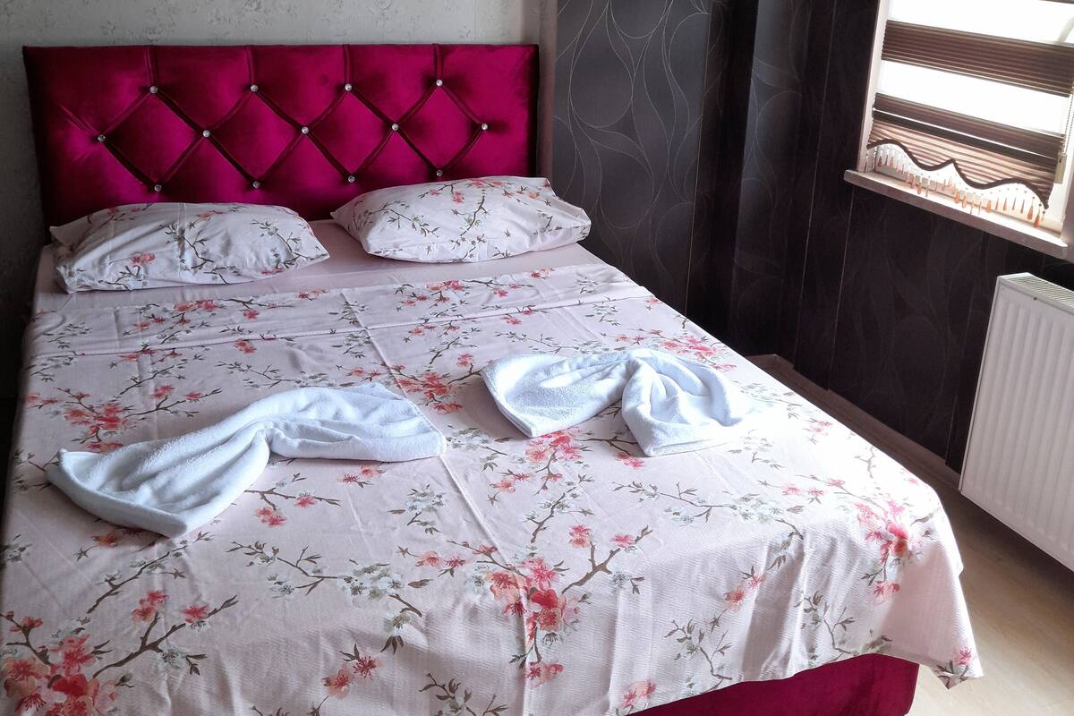 Ein Bett mit blumigem Überwurf, zwei Kissen und einem roten Kopfteil.