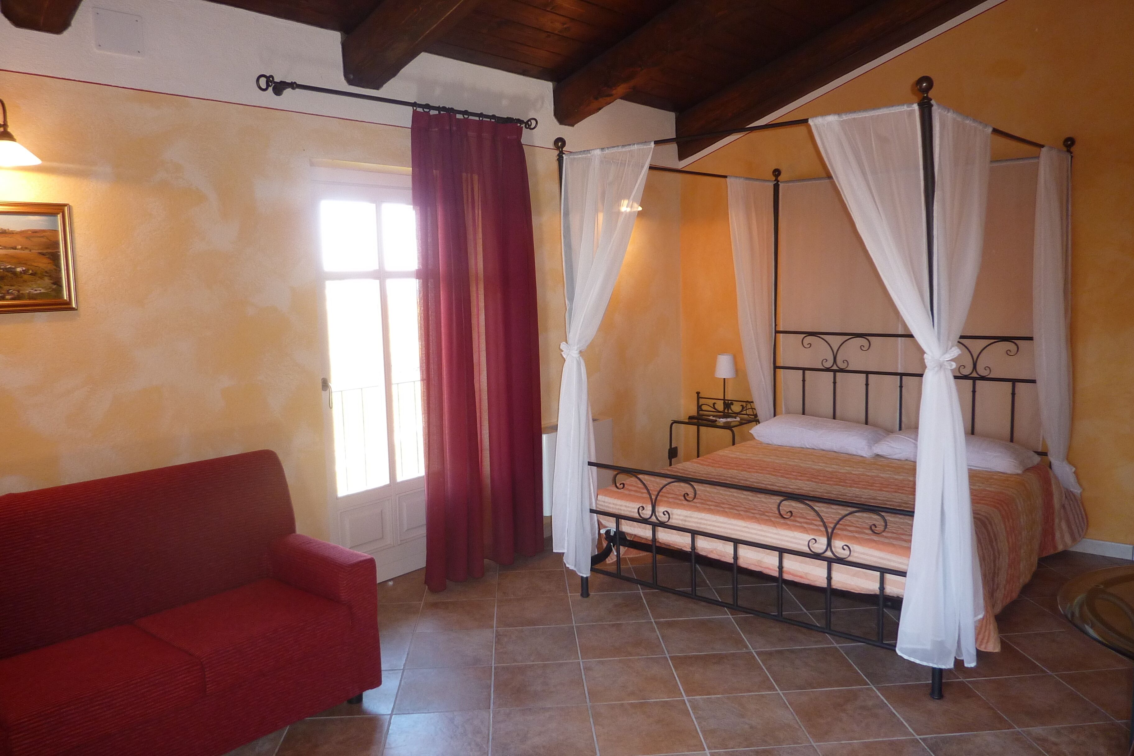 A bedroom with a four-poster bed, a red sofa, and a window with curtains.