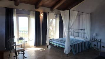 A bedroom with a four-poster bed, a glass table, and a chair.
