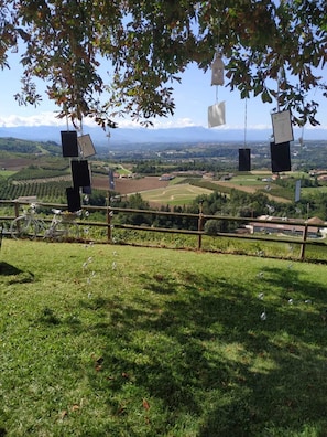 Zona verde con una bicicleta y una valla, con vistas a un valle con campos y montañas a lo lejos.