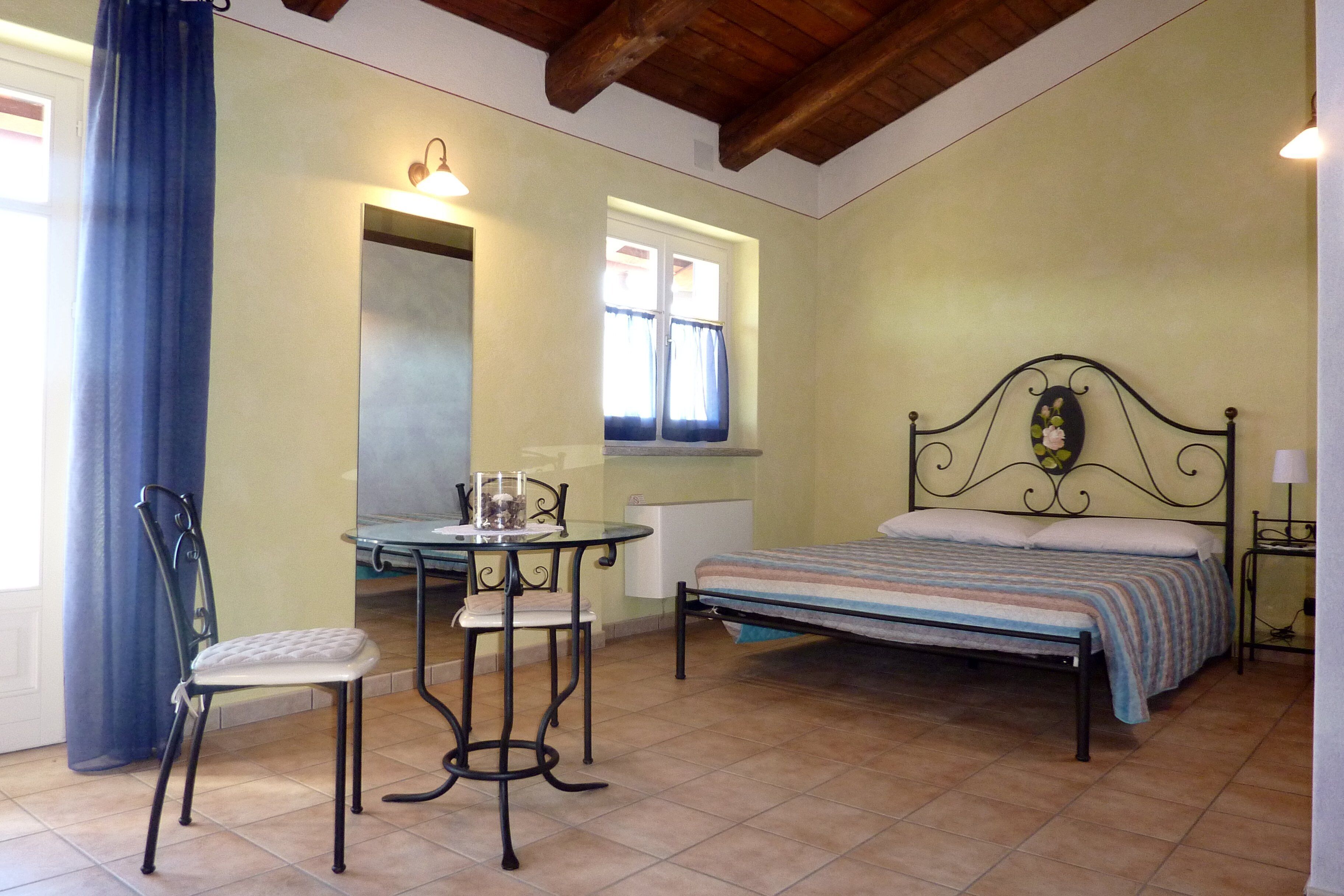 Un dormitorio con cama, una mesita y una silla, una ventana con cortinas y techo de madera.