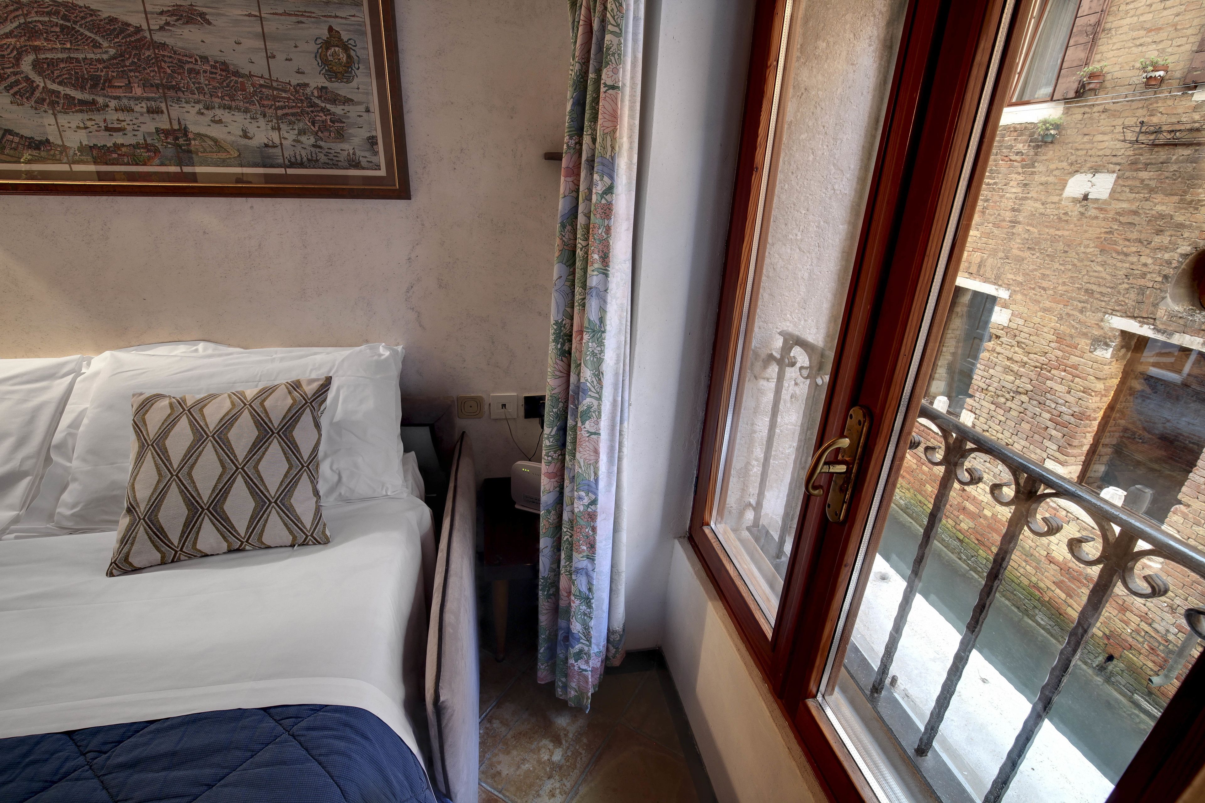 A bedroom with a bed, a window with a view of a brick building, and a curtain.
