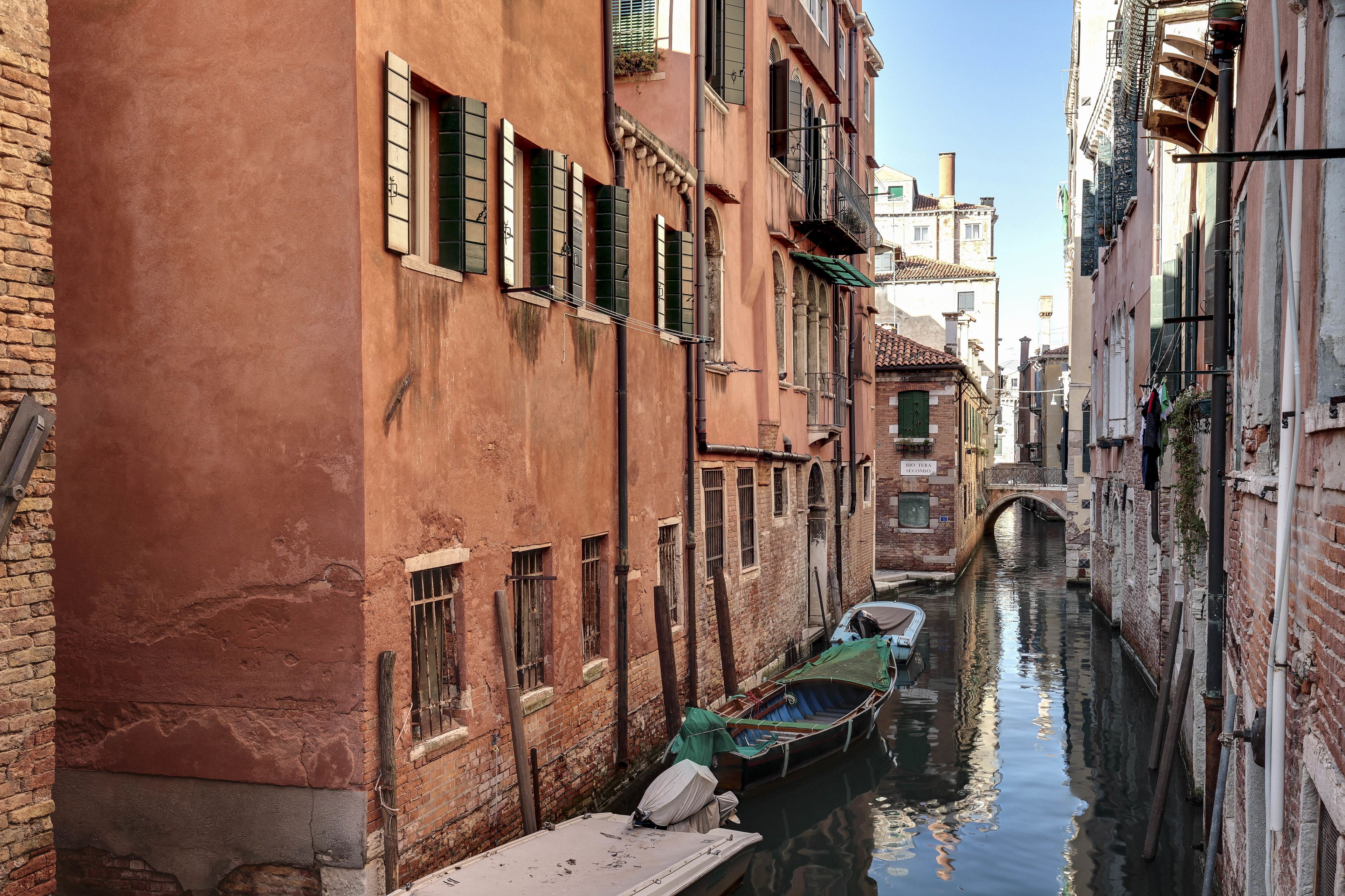 A narrow canal with boats docked along the sides, surrounded by historic buildings with brick facades and arched windows.