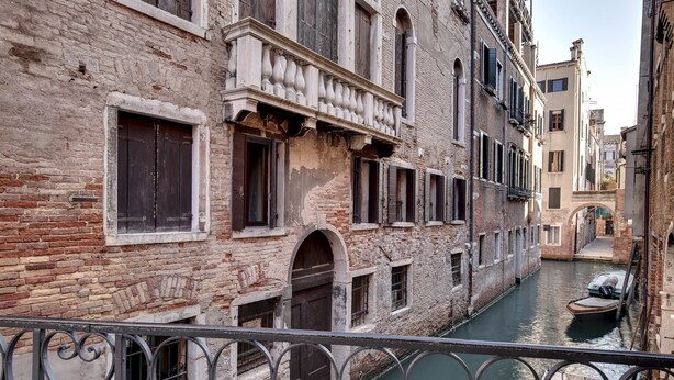 A narrow canal in a historic Venetian district with buildings featuring arched windows and balconies. - Canal View Suite in Rialto by Wonderful Italy (Venice)