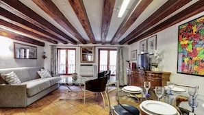 A living room with a sofa, chairs, a dining table set with plates and glasses, a television, and a colorful painting on the wall. - Canal View Suite in Rialto by Wonderful Italy (Venice)