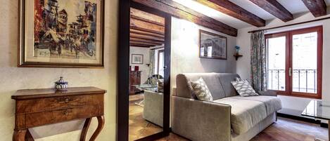 A living room with a sofa, a wooden side table, a mirror, and a painting on the wall.