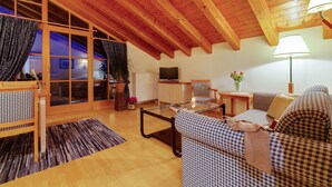 A cozy living room with a high wooden ceiling, a glass coffee table, checkered sofas, a television, and a potted plant.